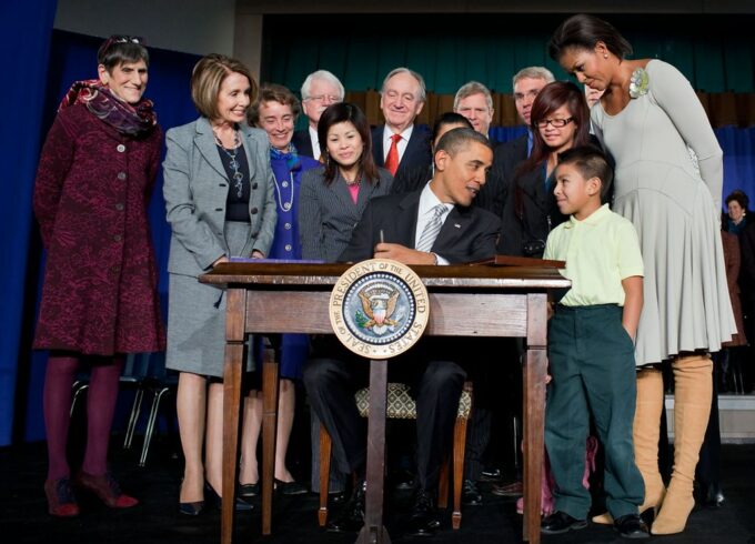 President Barack Obama signs the Healthy Hunger-Free Kids Act with Michelle Obama, Nancy Pelosi, Rosa DeLauro and a small child around him.