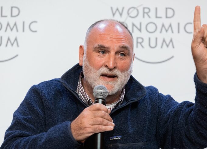 A photograph of humanitarian and chef José Andrés speaking at the World Economic Forum. He is wearing a navy blue patagonia fleece, donning a beard and holding a microphone and pointing a finger in the air.
