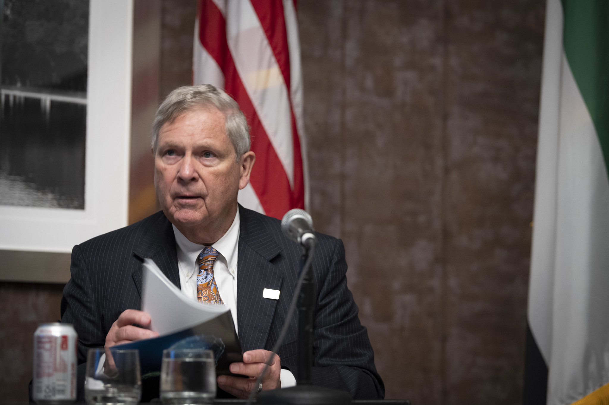 Agriculture Secretary Tom Vilsack sits at a table before a microphone against a backdrop of an American flag and United Arab Emirates flag at the AIM for Climate Summit in Washington.