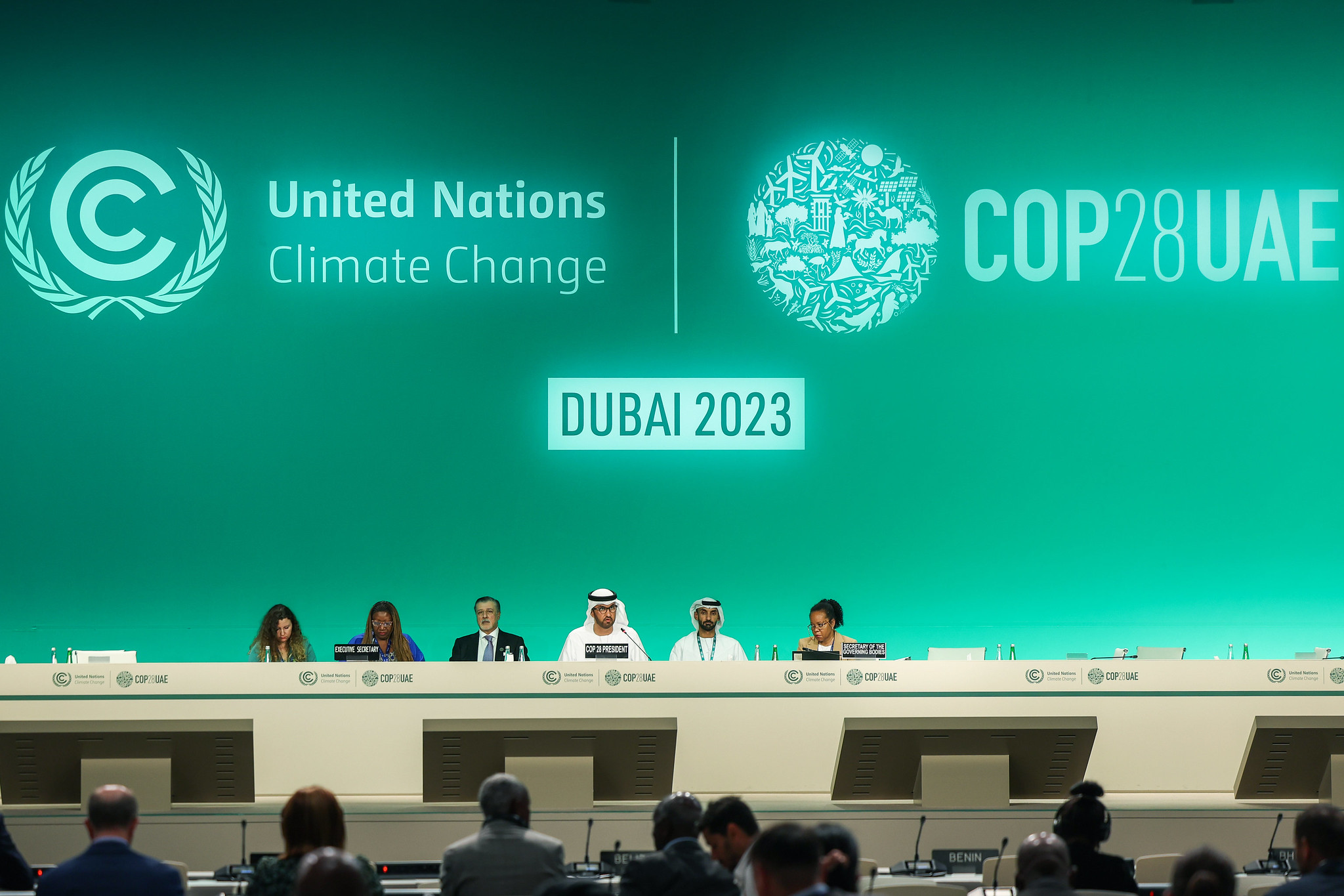 A green screen reads: United Nations Climate Change and COP28UAE - Dubai 2023. Six delegates are seated on a panel style set up underneath the large screen.