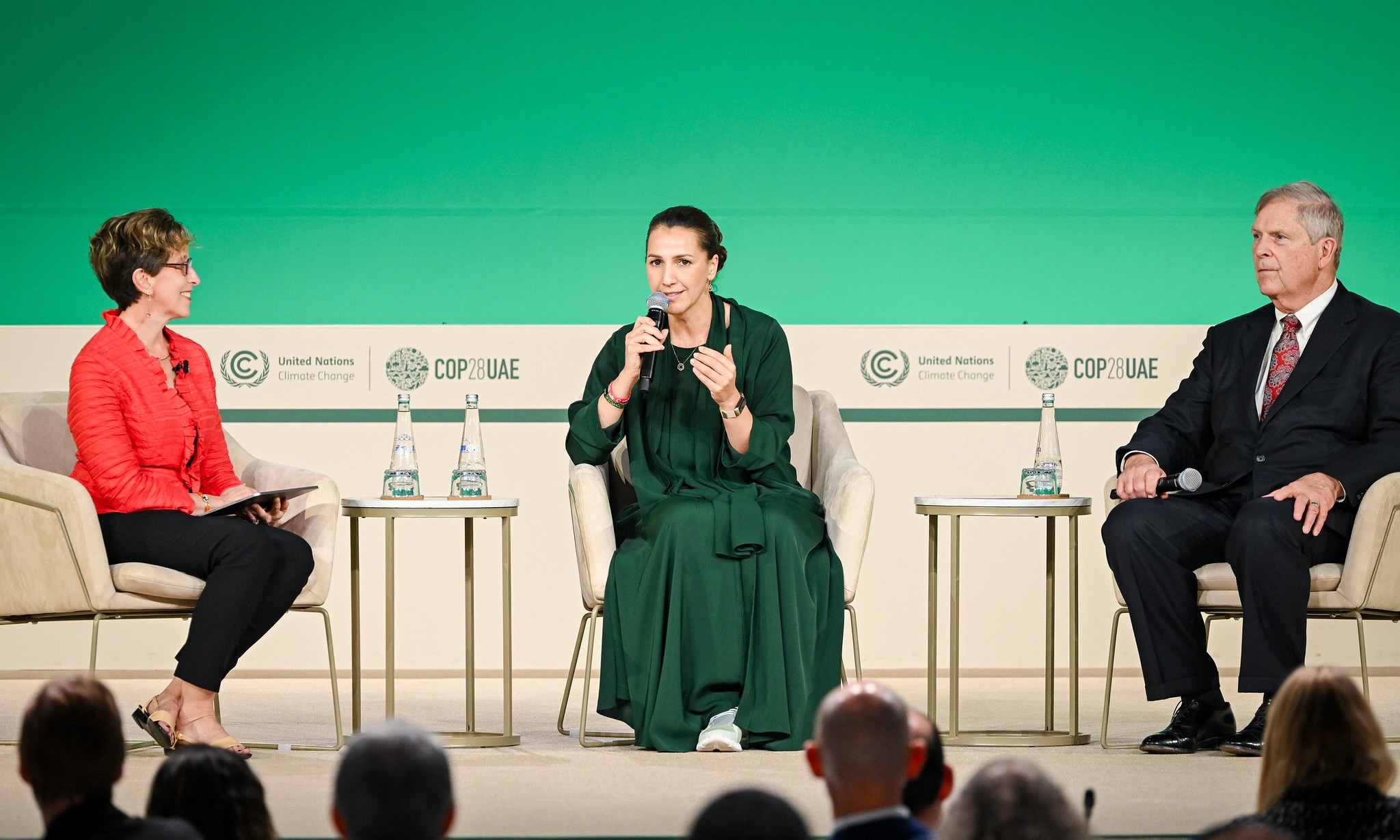 Diane Holdorf, Executive Vice President, WBCSD, USA, H.E. Mariam bint Mohamed Saeed Al Meheiri, UAE Minister of Climate Change and Environment and Tom Vilsack, Secretary of Agriculture, USA sit in chairs during a panel discussion against a green backdrop at the U.N. climate talks in Dubai.