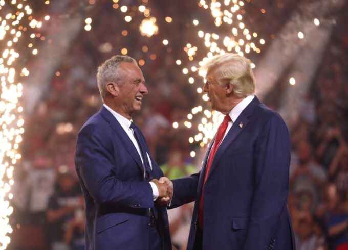 A photograph of Robert F. Kennedy Jr. and former President Donald Trump on stage in Glendale, Ariz., with fireworks behind them.