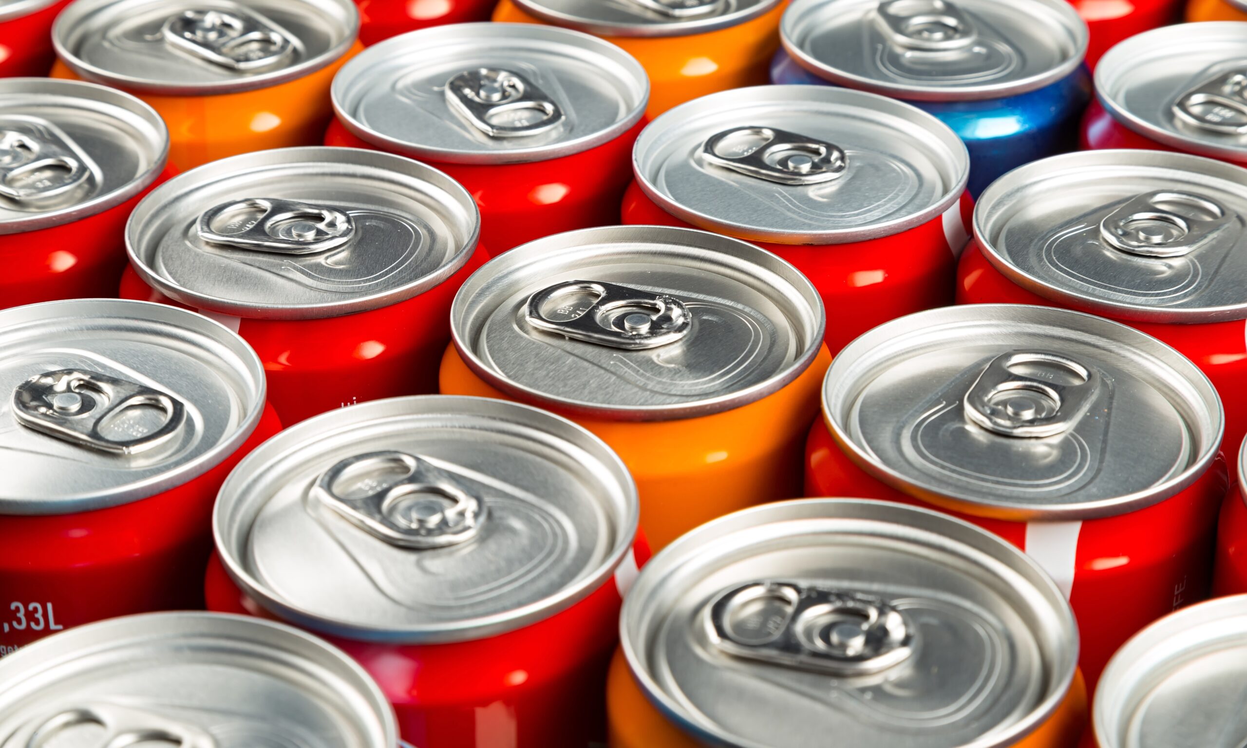 A close up photo of the tops of aluminum soda cans. The cans are orange, red and there is one that is blue.