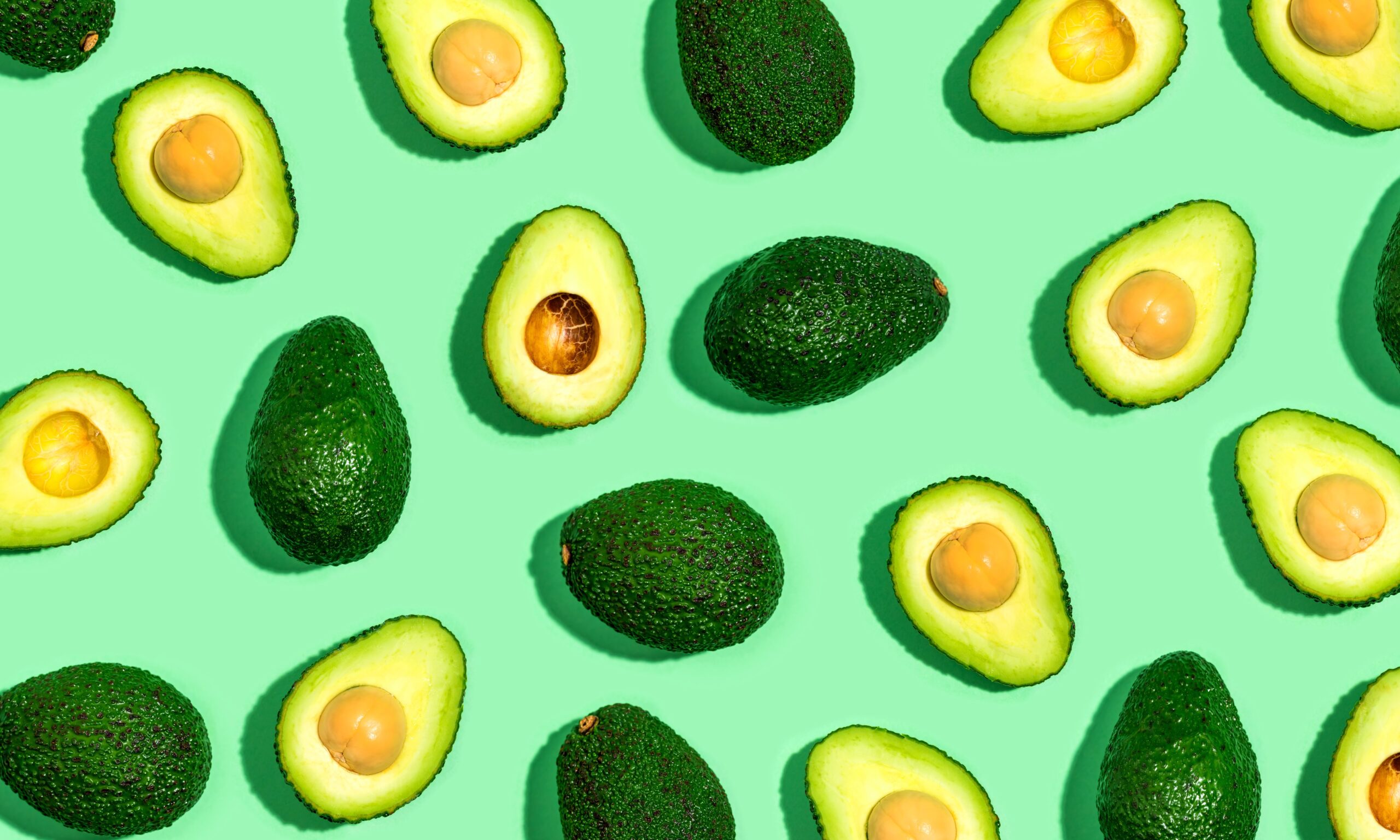 Light green background features many avocados halved some face up and some face down.