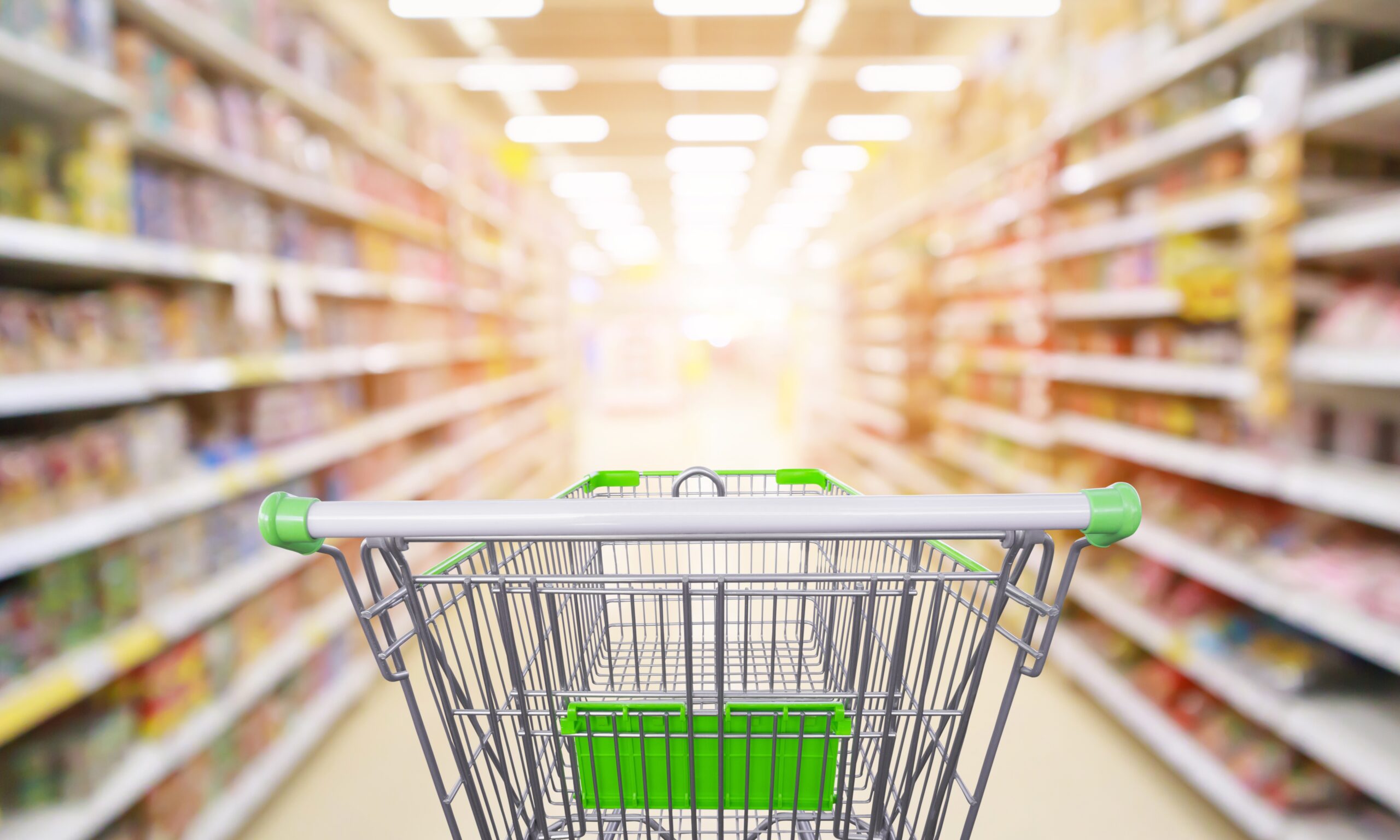 Photo of supermarket aisle product shelves interior blur background with empty shopping cart in the center.