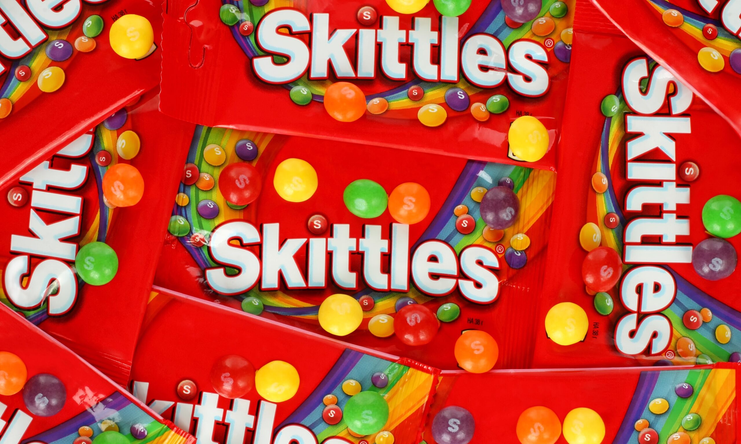 A pile of red bags of Skittles, pictured up close.