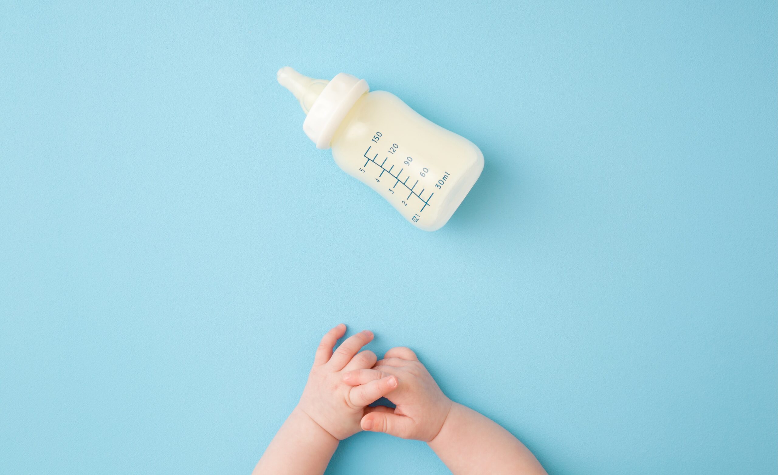 Baby hands folded in front of a bottle of formula on its side.