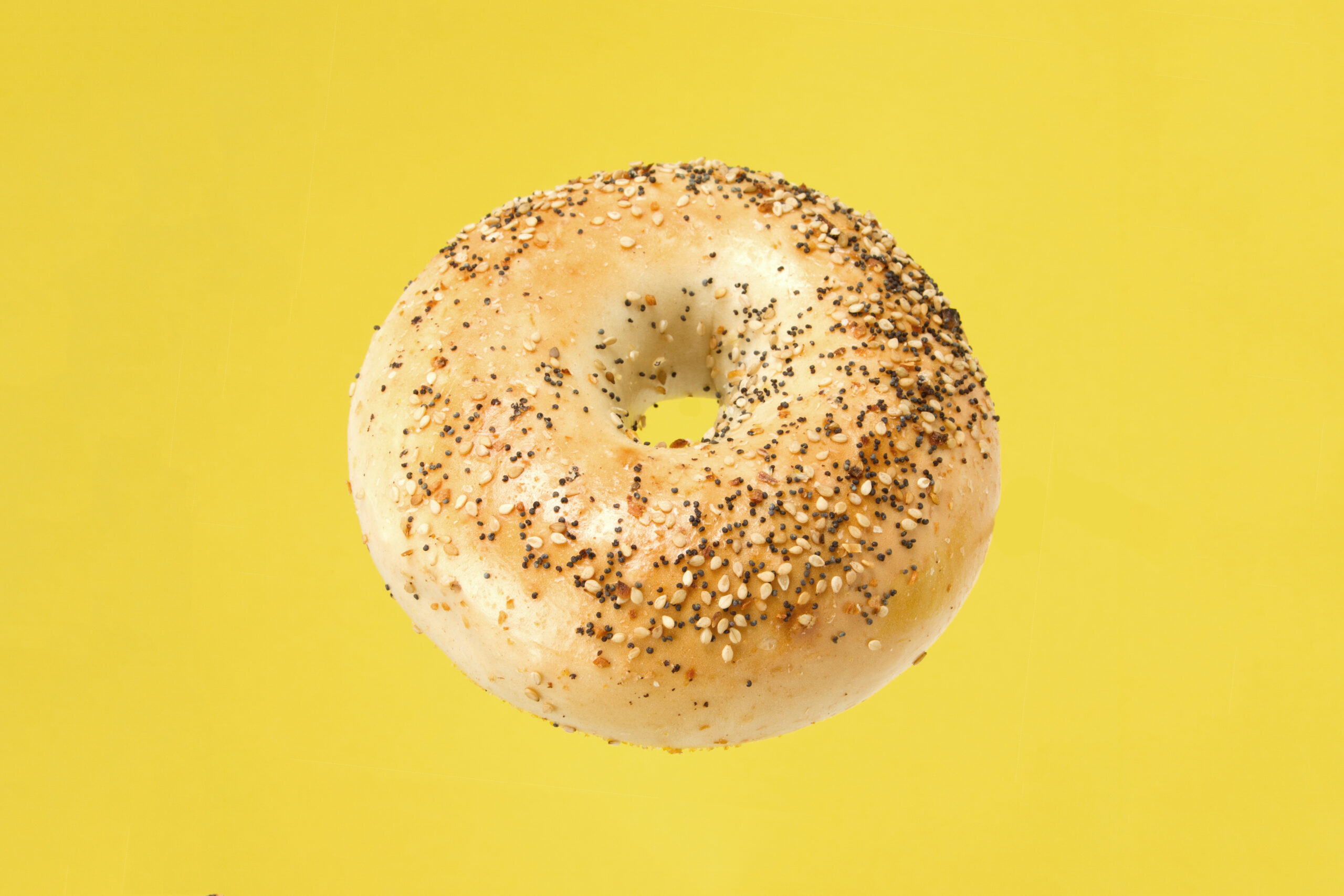 Everything bagel pictured in the center of a pure yellow backdrop.