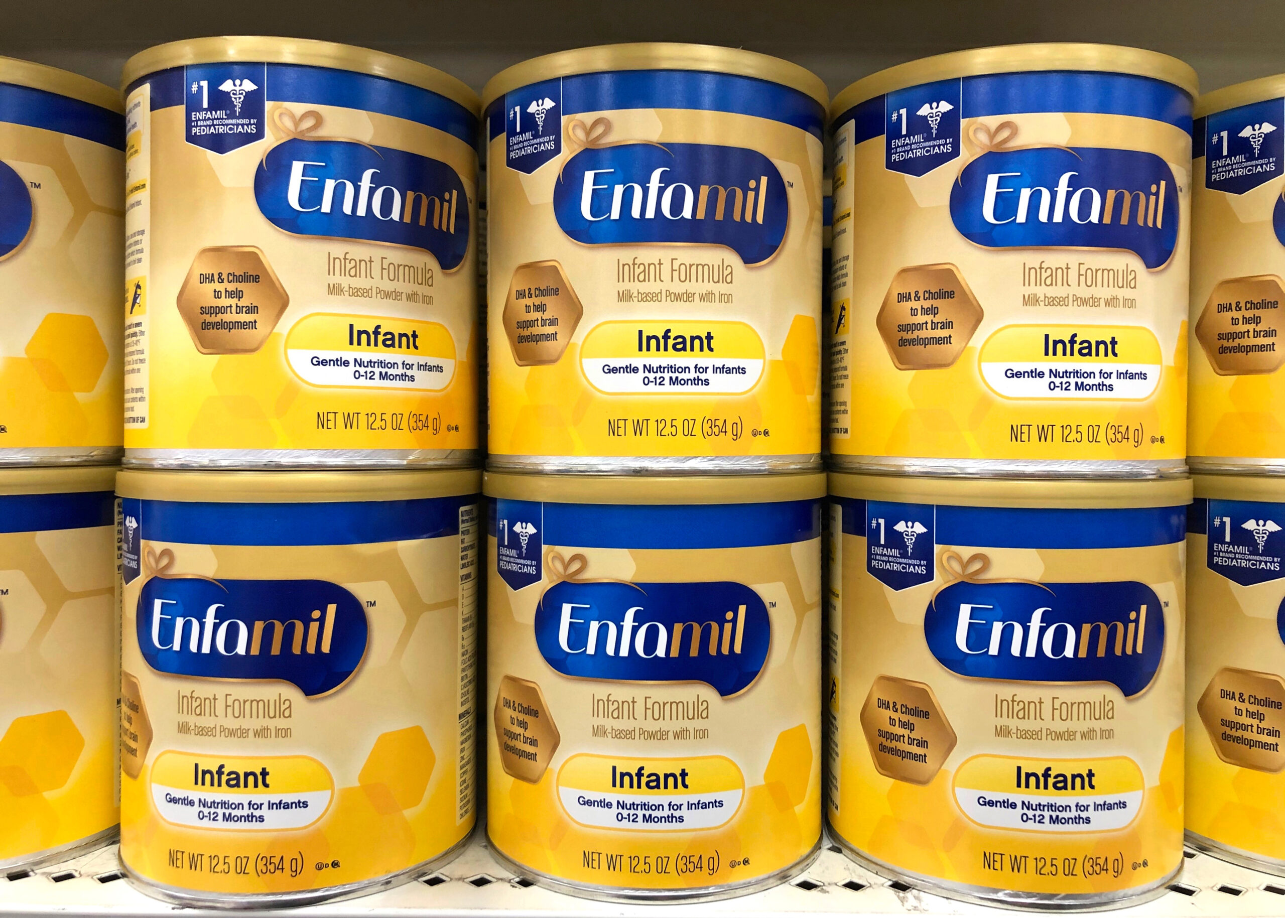 A close up view of yellow Enfamil infant formula cans stacked on a retail shelf.