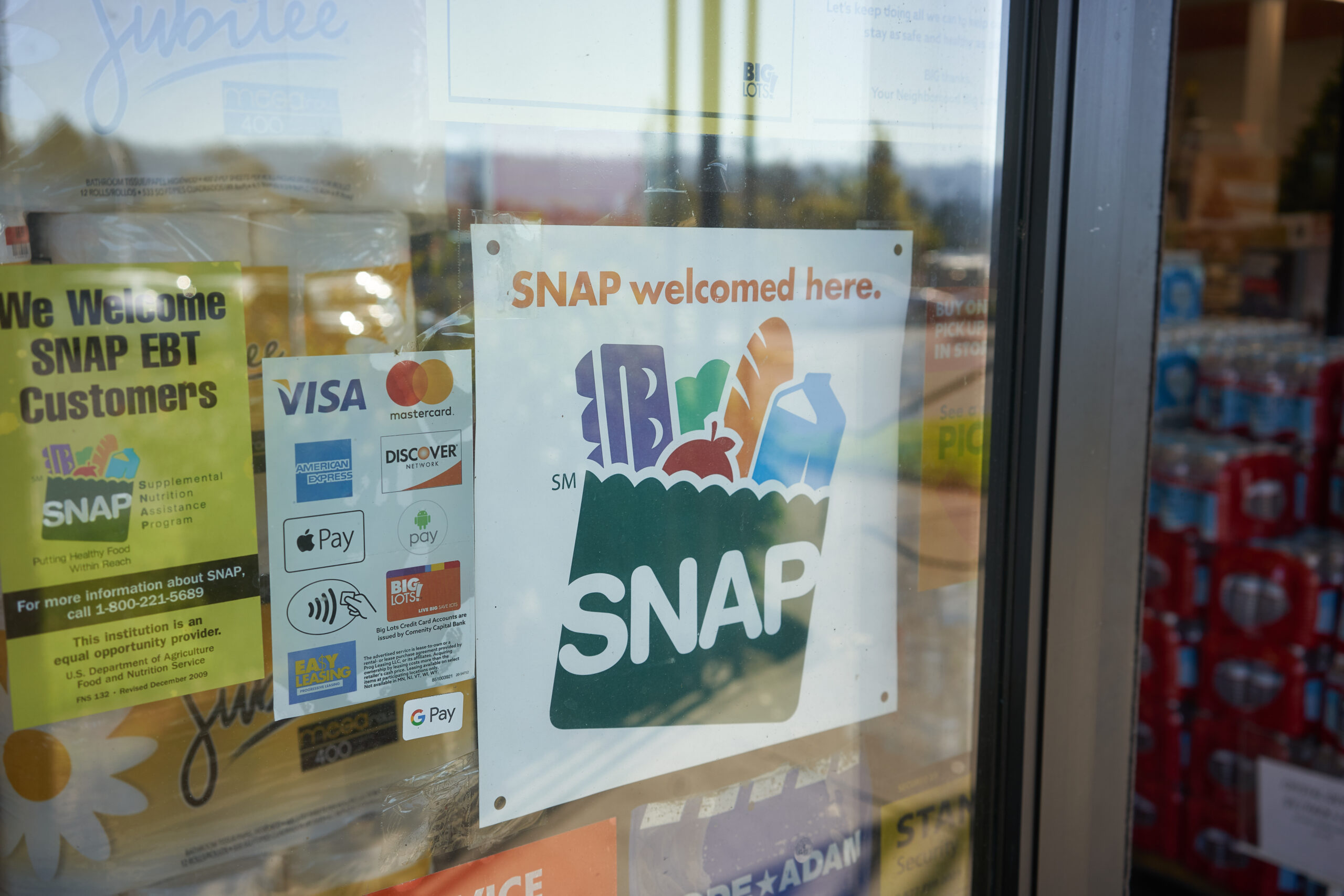 A photograph of a grocery store window with a sign indicating that SNAP benefits are welcomed.