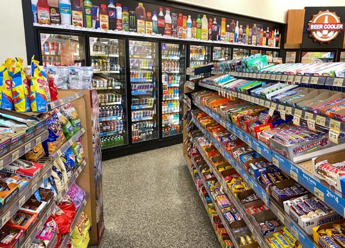 A photo of an aisle of a convenience store - the background is a cold case with soft drinks and beer.