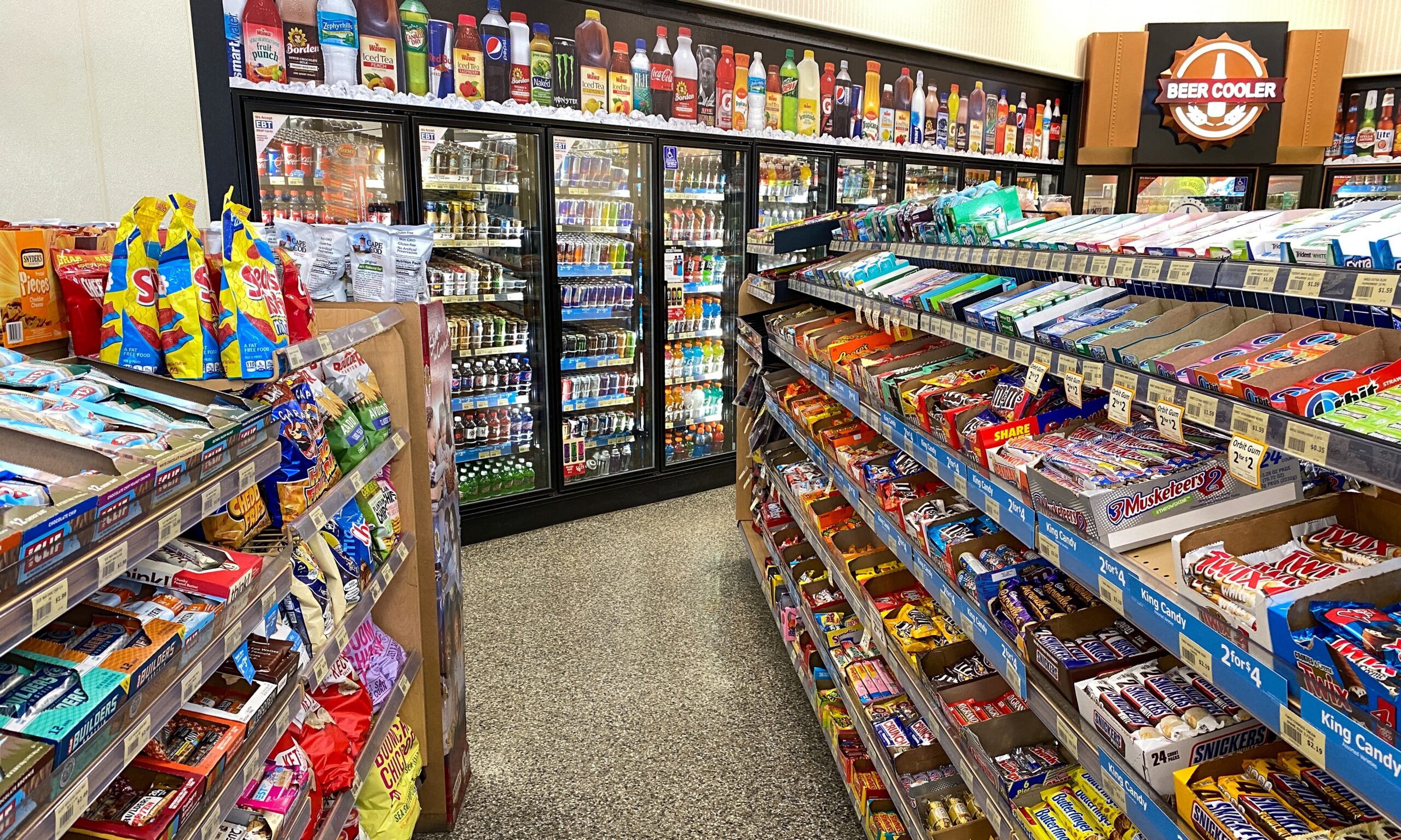 A photo of an aisle of a convenience store - the background is a cold case with soft drinks and beer.