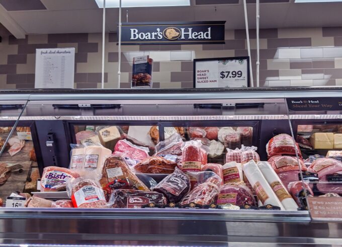 A photograph of a deli meat counter full of meats with a Boar's Head sign hanging above it.