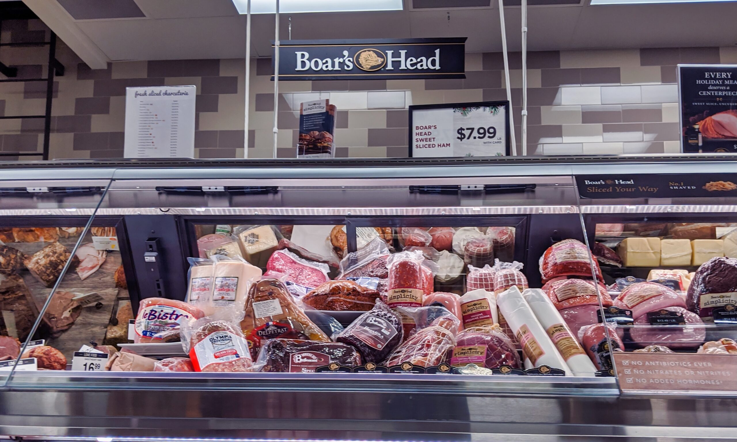 A photograph of a deli meat counter full of meats with a Boar's Head sign hanging above it.