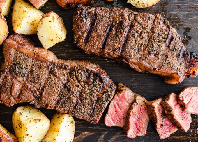 A close up photo of two steaks cut up and roasted potatoes on a cutting board.