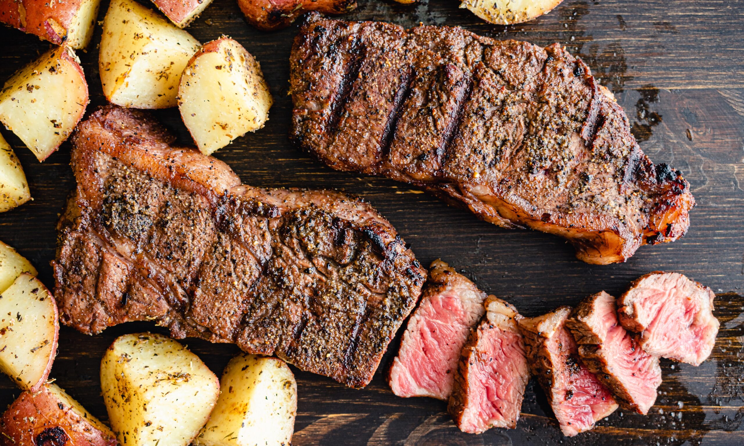 A close up photo of two steaks cut up and roasted potatoes on a cutting board.