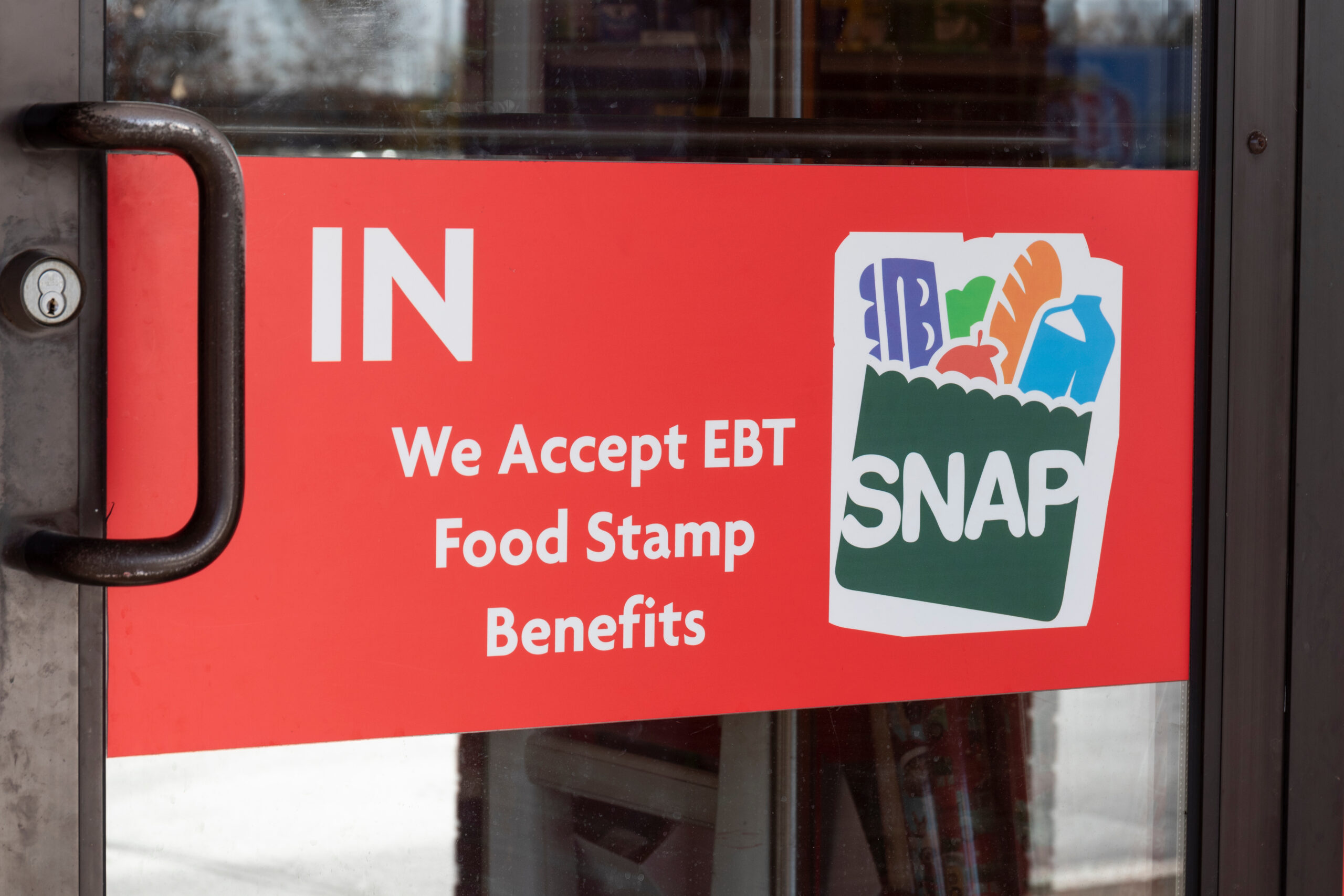 Zoomed in on a glass door to a store. The sign on the door says We accept EBT, food stamp benefits."