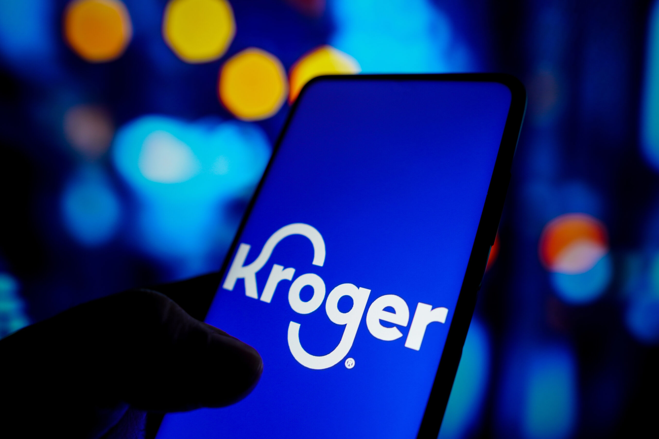 The Kroger logo appears on a smart phone against a blue backdrop.
