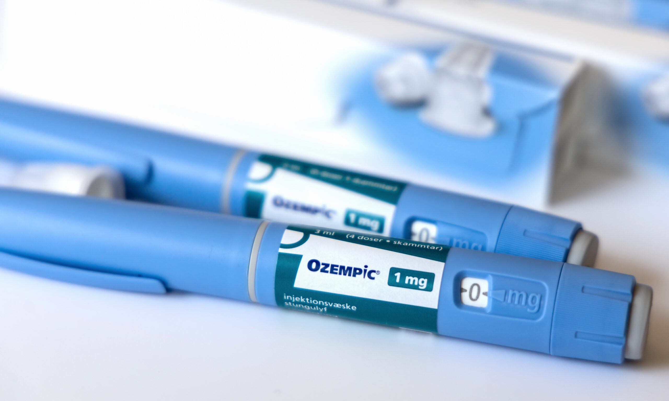 A close up photo of two blue Ozempic pens with boxes in the background (blurred out).