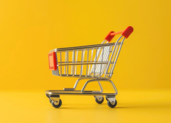 A toy metal shopping cart sits in the center of an all yellow background.