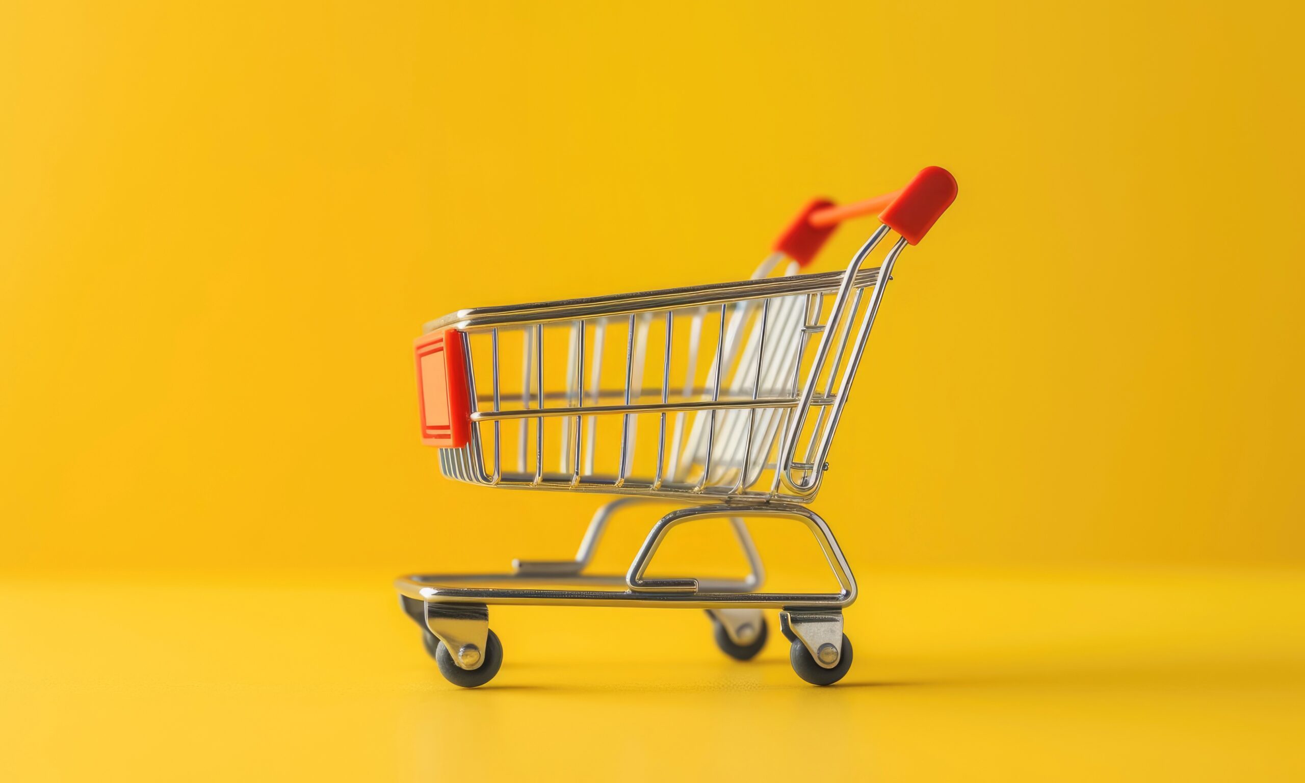 A toy metal shopping cart sits in the center of an all yellow background.