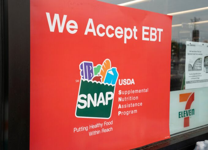 A photograph of a red sign on a 7 Eleven door that says "We Accept EBT" with the USDA SNAP logo on it.