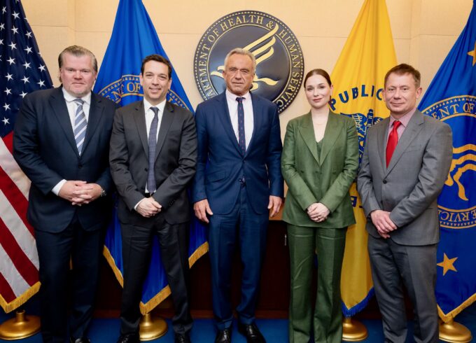 Four infant formula executives stand with Robert F. Kennedy Jr. at HHS in front of various flags.