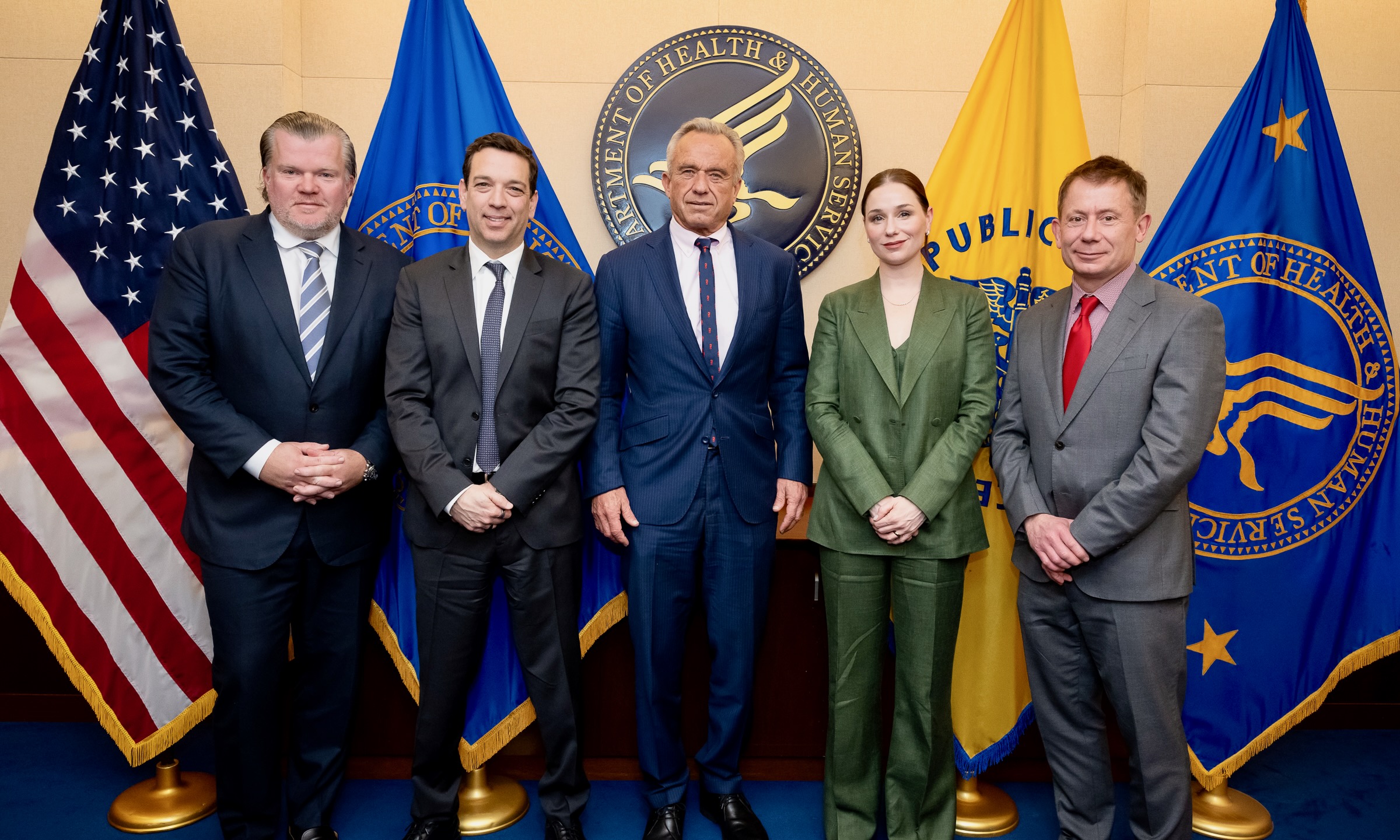 Four infant formula executives stand with Robert F. Kennedy Jr. at HHS in front of various flags.