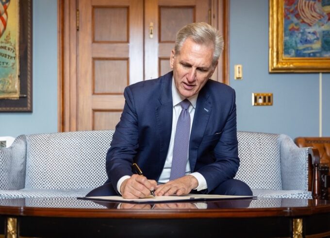 House Speaker Kevin McCarthy sits on a pale blue couch signing a bill on a coffee table in his office. Source: Twitter.