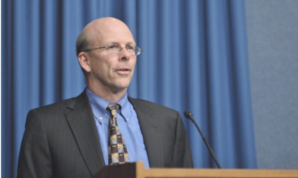 James Jones, former EPA official, standing at a podium against a blue curtain.