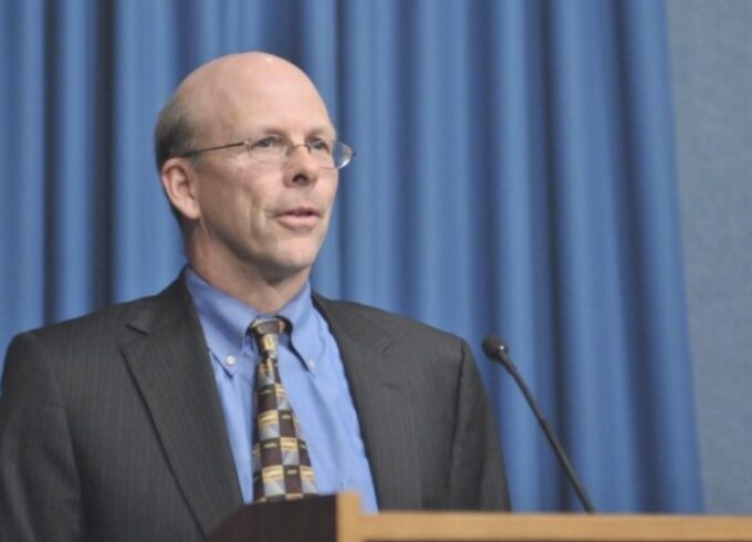 James Jones, former EPA official, standing at a podium against a blue curtain.